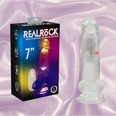 A clear, realistic RealRock Wireless Rechargeable LED Vibrating With Balls 7" dildo by Shots America stands by its box, featuring vibrant colors and a shiny pastel background, with the product name displayed on the packaging.